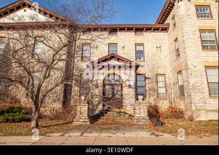 Gli storici appartamenti Rountree Hall di Platteville, Wisconsin, mostrano un'abbandono invernale con foglie su scale sotto il cielo azzurro. Foto Stock