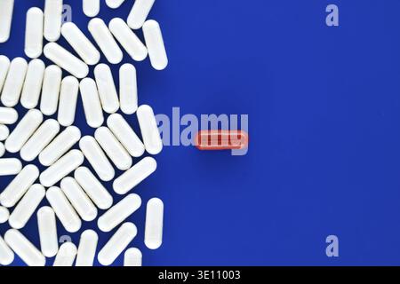Concetto medico-farmaceutico minimale con pillole bianche sparse sulla superficie blu e singola pillola rossa fuoco di disegno, simbolicamente rappresentativo unico Foto Stock