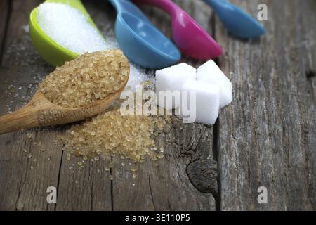 Set di misurini colorati in plastica con zucchero di canna e zucchero bianco versato su una superficie rustica in legno Foto Stock