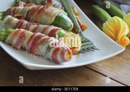 Patatine grigliate di zucchine avvolte in una pancetta su un piatto bianco Foto Stock