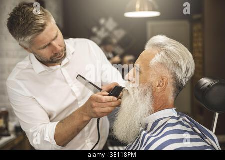 Bell'uomo anziano che ottiene lo styling e la rifinitura della sua barba nel barbiere Foto Stock