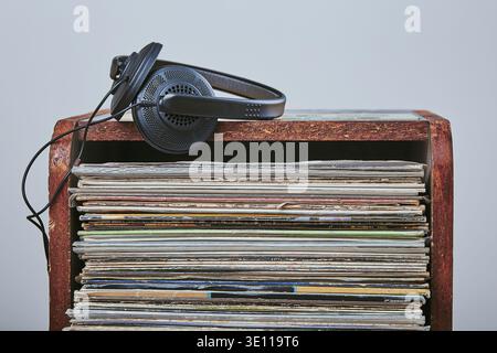 Una pila di molti dischi in vinile nero e cuffie posizionate in cima alla pila. Persone since, momenti reali, situazioni autentiche Foto Stock