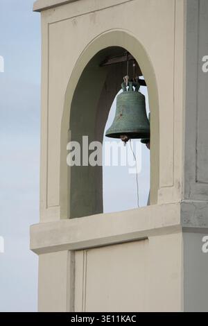 Campana della chiesa appesa all'interno di un arco a torre contro una nuvolosa sky.in Rodi, Grecia. Foto Stock