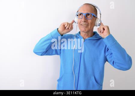 Studio shot di pensosa felice bald senior uomo sorridente mentre ascolti la musica e indossando occhiali contro uno sfondo bianco Foto Stock