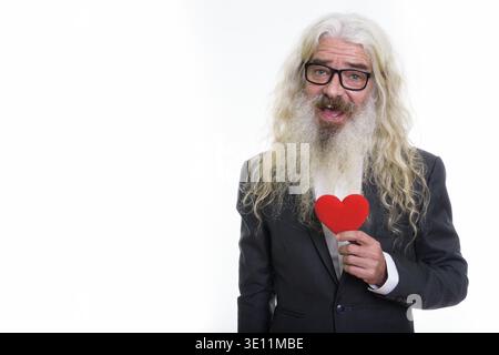 Studio shot di felice senior barbuto imprenditore sorridente tenendo cuore rosso Foto Stock