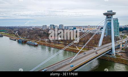 Ampia vista aerea del ponte UFO a Bratislava che attraversa il Danubio con il lungofiume e lo skyline urbano; ideale per viaggi, trasporti, editoriale, touri Foto Stock