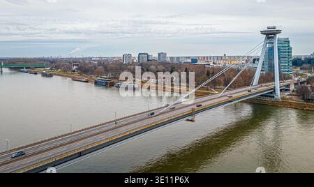 Ampia vista aerea del ponte UFO a Bratislava che attraversa il Danubio con il lungofiume e lo skyline urbano; ideale per viaggi, trasporti, editoriale, touri Foto Stock