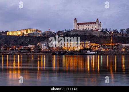 Vista al crepuscolo del castello di Bratislava sopra il Danubio con luci e riflessi luminosi della città in Slovacchia; ideale per viaggi, turismo, editoriale, herita Foto Stock