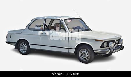 Elegante donna anziana alla guida di una classica BMW 2002 bianca su sfondo bianco Foto Stock