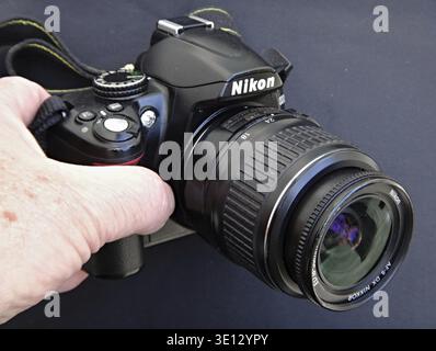 Mano che regge una fotocamera DSLR Nikon D3000 con un obiettivo Nikkor da 55 mm Foto Stock