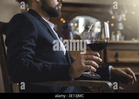 Uomo che indossa un abito nero con un bicchiere di vino rosso Foto Stock
