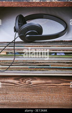 Una pila di molti dischi in vinile nero e cuffie posizionate in cima alla pila. Persone since, momenti reali, situazioni autentiche Foto Stock