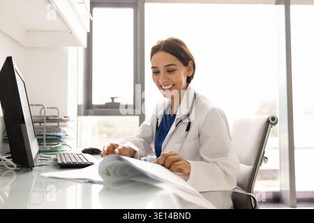 Giovane medico donna in uniforme che lavora seduto al tavolo del posto di lavoro Foto Stock