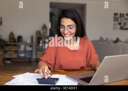 Sorridente giovane donna in occhiali che calcolano le finanze a casa Foto Stock