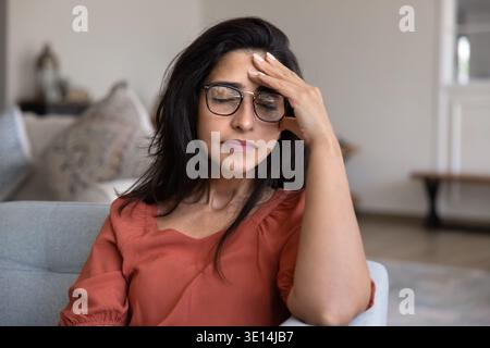 Donna stressata con gli occhi chiusi che toccano la fronte seduta all'interno Foto Stock