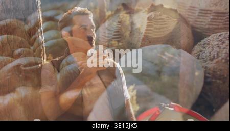 Camper maturo inclinato che tiene la tazza di metallo vicino al petto in un campeggio roccioso, indossa il gilet, la copertura del pane Foto Stock