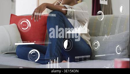 Donna seduta in Blue-jeans, top a maniche lunghe, ginocchia sul divano del salotto, sovrapposizioni HUD, tazza sfocata Foto Stock