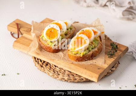 Due fette di lievito madre croccante ricoperte di crema di avocado e uova sode di media consistenza. La luce naturale soffusa mette in risalto le texture rustiche della Foto Stock