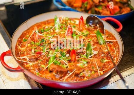 Saporito stufato di manzo al curry indiano che presenta sapori ricchi, carne tenera e spezie aromatiche, guarnito con peperoni verdi e rossi a fette e fresco Foto Stock