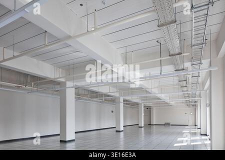 Ampio pavimento vuoto per uffici con colonne bianche e servizi a soffitto a vista. Foto Stock