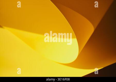 Carta gialla che crea un bellissimo motivo astratto di curve, luci e ombre Foto Stock