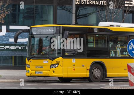 Germania Berlino 14 marzo 2026. Un autobus pubblico giallo BVG attraversa una strada di Berlino accanto ai moderni edifici in vetro. Il veicolo rappresenta la p Foto Stock