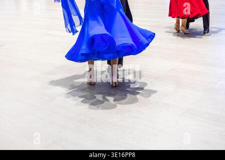 Una coppia danzante danzerà un programma standard con un abito blu e un cappotto nero, e con un abito rosso e un cappotto nero Foto Stock