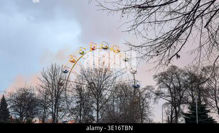 La ruota panoramica nel parco cittadino è illuminata dai raggi del sole che tramonta. La calda luce solare riflette la struttura metallica della guida contro il Foto Stock