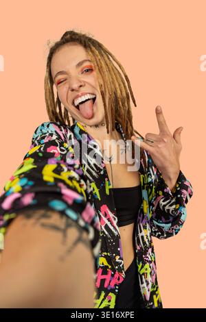 Giovane donna con dreadlock, tatuaggi e giacca colorata in posa per un selfie Foto Stock