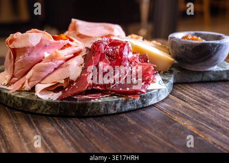 Un delizioso tagliere di salumi con un assortimento di prosciutto e formaggio stagionato, disposto ad arte su un piatto di marmo scuro. Perfetto per piatti gourmet Foto Stock