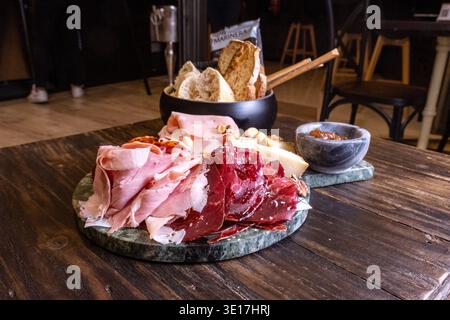 Un delizioso tagliere di salumi con una vasta gamma di prosciutto stagionato, pane e accompagnamenti disposti su un rustico tavolo in legno. Perfetto per piatti gourmet Foto Stock