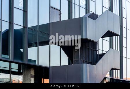 Un'elegante e contemporanea scala in metallo avvolge l'esterno di un moderno edificio in vetro, mostrando innovazione architettonica e design urbano Foto Stock