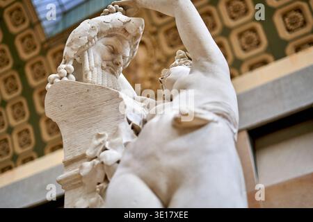 Una vista ravvicinata dall'angolo basso di un'intricata scultura in marmo bianco esposta all'interno di un museo. La statua classica presenta figure dettagliate... Foto Stock