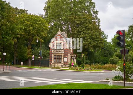 Un'affascinante e storica porta di ingresso in mattoni o un piccolo cottage si trova all'angolo di una strada a Parigi, in Francia, circondato da lussureggianti alberi verdi.... Foto Stock