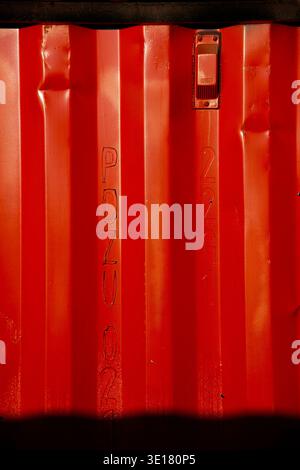 Primo piano di una parete rossa del contenitore di spedizione che mostra i numeri di serie verticali in rilievo e l'hardware industriale. Foto Stock