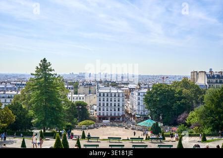 Una vista panoramica del paesaggio urbano di Parigi presa da un punto panoramico sopraelevato a Montmartre. Il primo piano presenta un parco paesaggistico con panchine verdi, Foto Stock