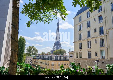 La Torre Eiffel si innalza sopra i classici condomini parigini in una luminosa giornata di sole con cielo blu e nuvole bianche Foto Stock