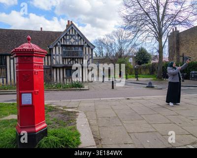 Una rara scatola a colonne vittoriana si erge in modo prominente su Church Lane nel Walthamstow Village, Londra, nel marzo 2026. Questa iconica cassetta per posta esagonale, progettata dall'architetto John Wornham Penfold e prodotta tra il 1866 e il 1879, è una delle poche "Penfolds" originali ancora in uso nella capitale. La scatola presenta un caratteristico cappuccio decorato con foglie di acanto, un bocciolo finale e palle decorative. Sullo sfondo si trova l'Ancient House, una casa con hall in legno di grado II* risalente al 1435 circa, che la rende uno dei più antichi edifici residenziali sopravvissuti di Londra Foto Stock