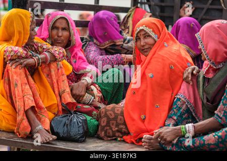 Diverse donne con i tradizionali veli arancioni e rosa siedono insieme su un veicolo a pianale a Pushkar Mela, impegnate in una conversazione durante il viaggio. Foto Stock
