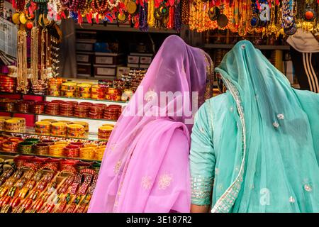 Due donne in veli viola e turchese traslucidi guardano un'ampia esposizione di bracciali in vetro e collane con perline in uno stand di Pushkar Mela. Foto Stock