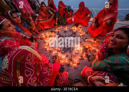 Un gruppo di donne in abito tradizionale siede accanto all'acqua al lago Pushkar, sistemando e accendendo numerose piccole lampade a olio sul terreno di pietra al crepuscolo. Foto Stock