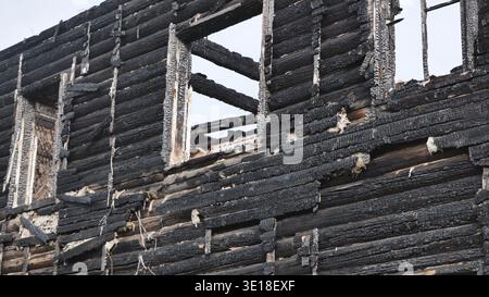 Esterno carbonizzato di una casa in legno bruciata con telai delle finestre vuoti Foto Stock