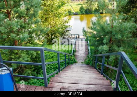 Scenografiche scale in legno che si snodano giù verso un'intima terrazza sul pondolino. La lussureggiante vegetazione estiva incornicia questa invitante fuga nella natura, perfetta per momenti sereni Foto Stock
