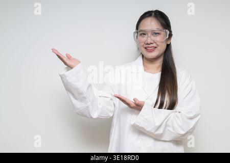 Ritratto di medico scienziato asiatico donna in camice da laboratorio che indossa occhiali di sicurezza su sfondo bianco posa con fiducia Foto Stock