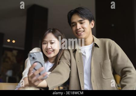 Ritratto di una giovane coppia asiatica felice che scatta selfie in un bar con smartphone Foto Stock