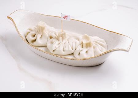 Tre gnocchi di khinkali tradizionali georgiani serviti in un piatto di ceramica. Ripieno di carne succoso avvolto in un impasto morbido. Cuisi nazionale classico e autentico Foto Stock