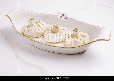 Gnocchi di khinkali tradizionali georgiani serviti in un piatto di ceramica, delicatamente guarniti con erbe aromatiche per una presentazione autentica e saporita Foto Stock