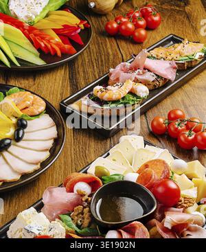 Delizioso assortimento di antipasti esposti su un tavolo di legno che comprende gamberi, affettati, formaggi, peperoni, pomodori, olive e verdure fresche. IDE Foto Stock