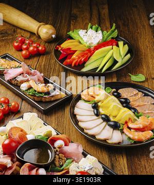 Delizioso assortimento di antipasti esposti su un tavolo di legno che comprende gamberi, affettati, formaggi, peperoni, pomodori, olive e verdure fresche. IDE Foto Stock