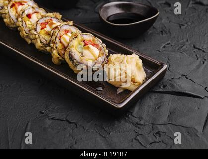 Un piatto propone sushi roll appena fatti ripieni di verdure e frutti di mare vivaci, accompagnati da fette di zenzero sottaceto e piccole ciotole di immersione Foto Stock